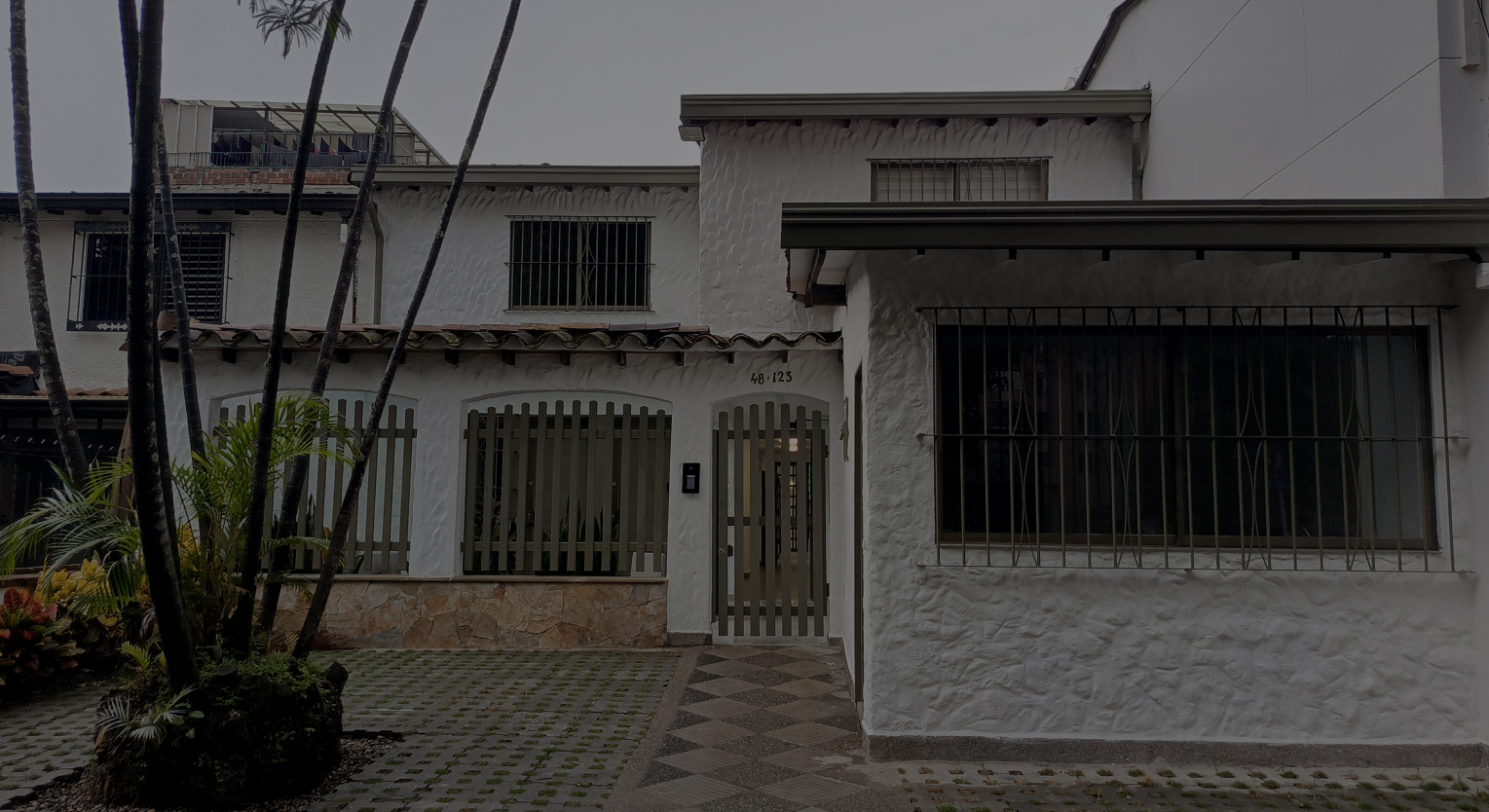Fachada de casa residencial con reja metálica y pequeño jardín frontal.